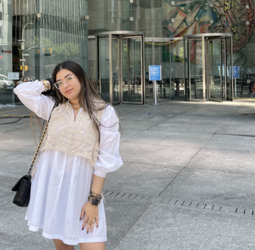 Subject is posing in a white dress in front of a glass structure.